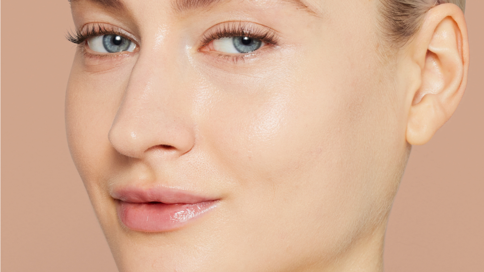 Krupni plan lica istog modela sa ujednačenim tonom kože, blistavim 'dewy' sjajem i umanjenim crvenilom nakon nanošenja Jane Iredale Skintuition tonirane kreme."